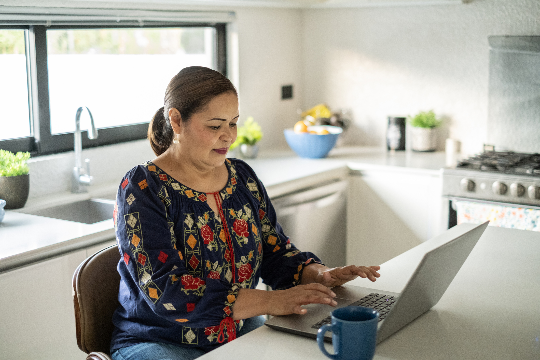 A woman sitting at a table using her laptop to access the wellness hub. 