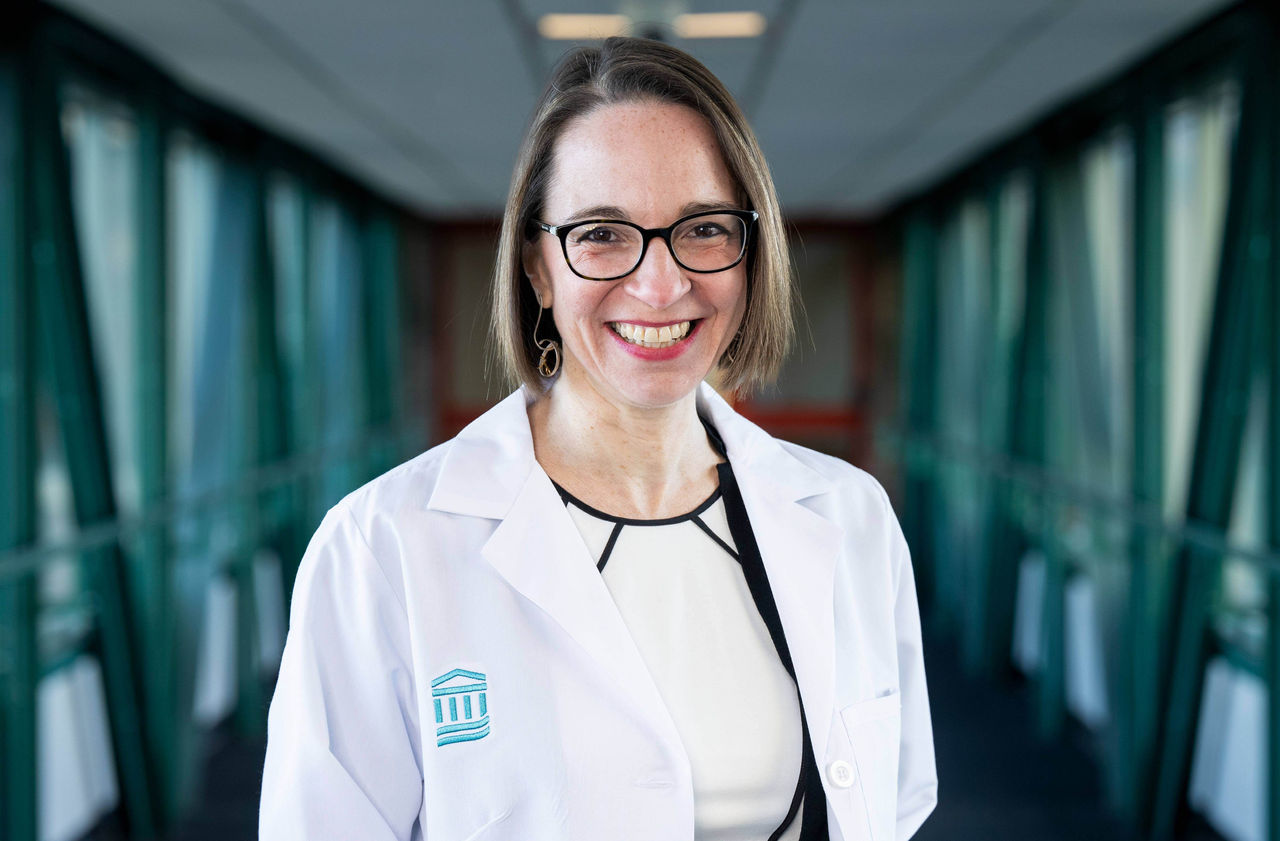 Woman with black glasses smiling in a white coat